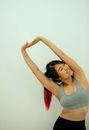 Positive Asian female in activewear stretching arms while practicing yoga and looking away against white wall