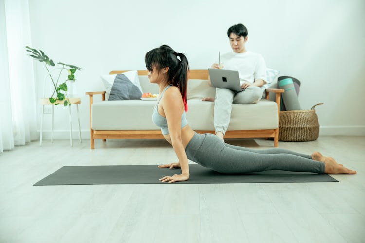 Woman Practicing Yoga And Man Using Laptop