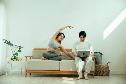 Free Full body of Asian male using laptop while happy female stretching body on sofa in light living room Stock Photo