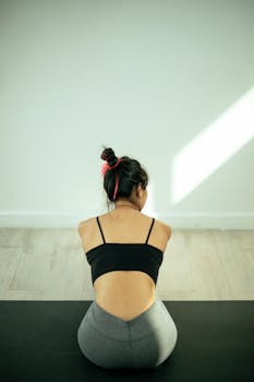 Back view of a woman practicing yoga indoors, promoting fitness and wellness.