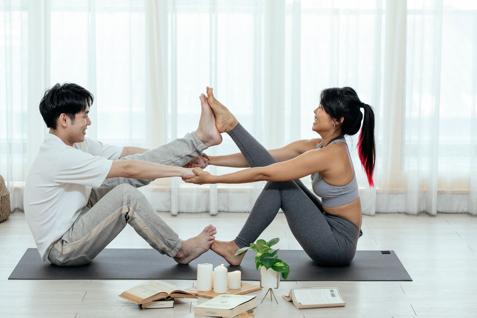 Couple practicing Naukasana boat pose together on a yoga mat indoors