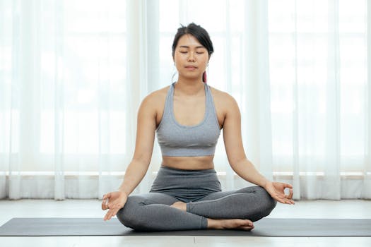 Asian woman meditating indoors on yoga mat, promoting fitness and wellness.