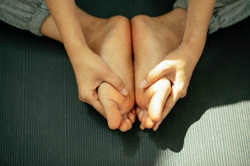 From above of crop anonymous barefooted female in sportswear sitting on mat and practicing Baddha Konasana pose during yoga session