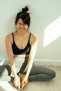 Cheerful Asian woman in activewear sitting on floor