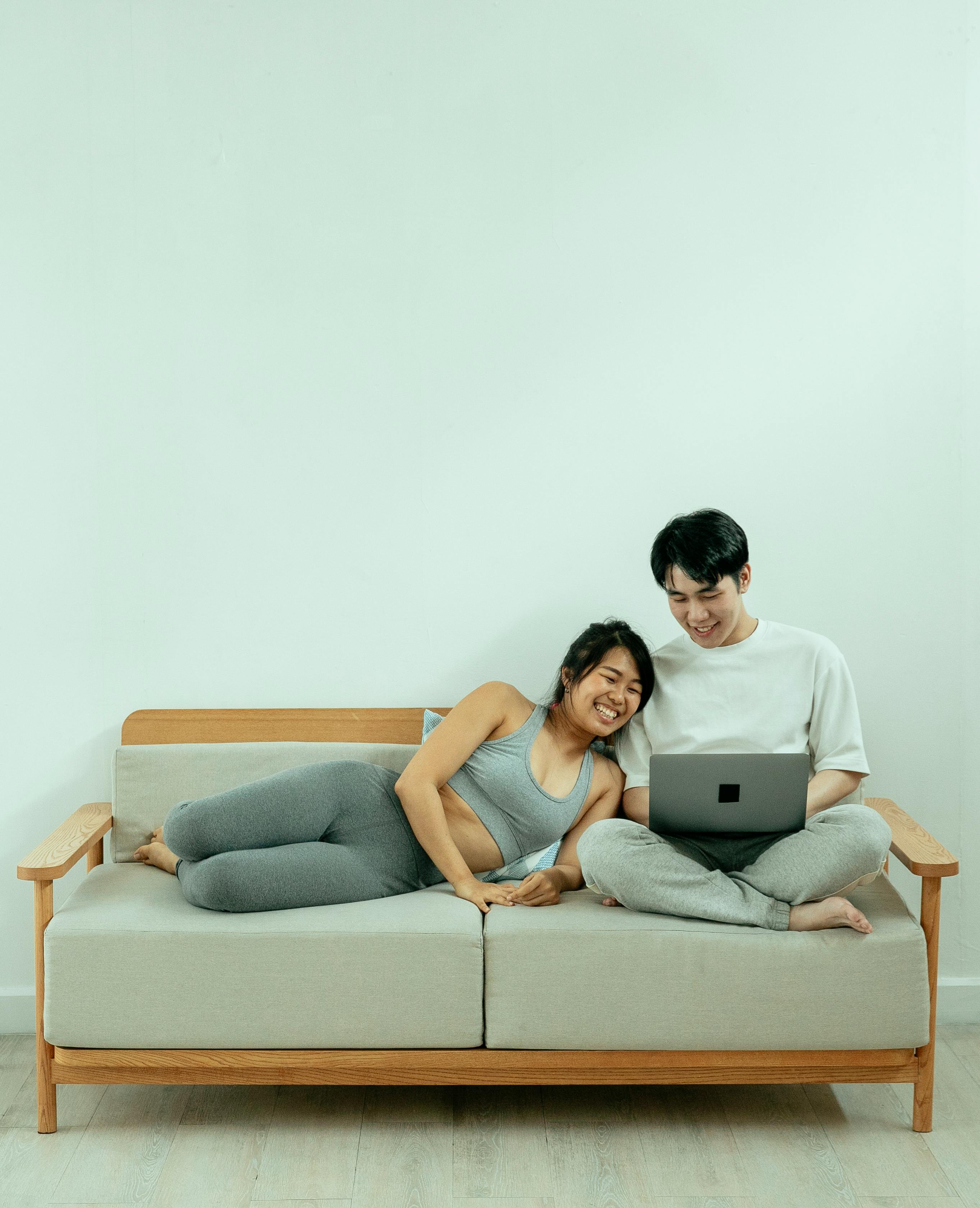 cheerful asian couple resting on sofa with laptop