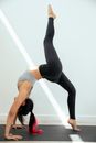 Side view of anonymous fit barefoot slim female in activewear performing Wheel pose or Urdhva Dhanurasana with raised leg during yoga session on floor against white wall