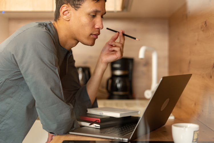 Man Holding A Pencil While Looking At The Laptop Screen 