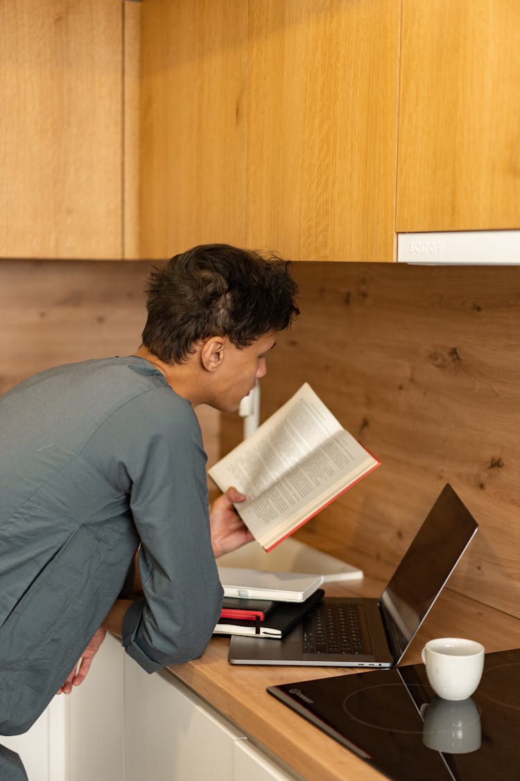 Man Reading Book While Leaning On Wooden Counter