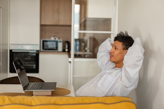A man in a white shirt relaxes with a laptop in a contemporary kitchen environment, enjoying leisure time.