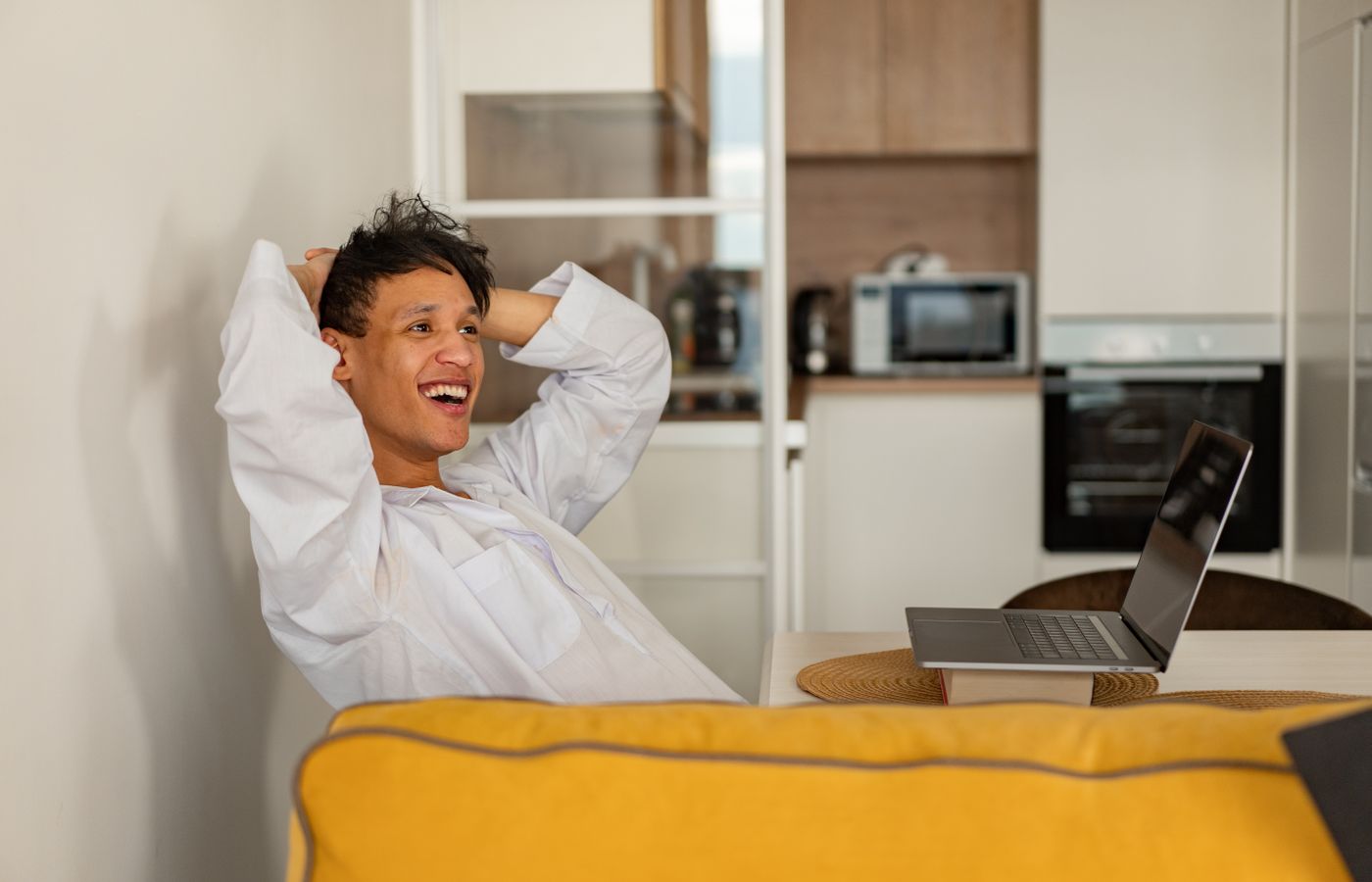 Casually dressed man enjoying leisure time at home with an open laptop, expressing happiness and relaxation.