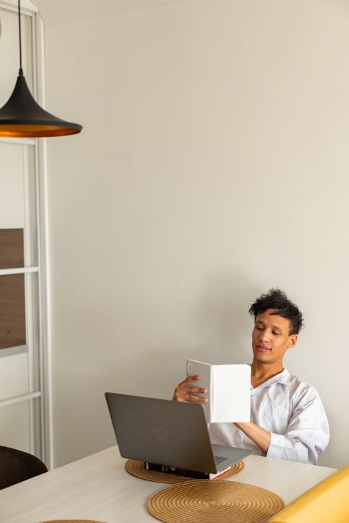 Free A young man studies in a minimalist home office with a laptop and book. Stock Photo