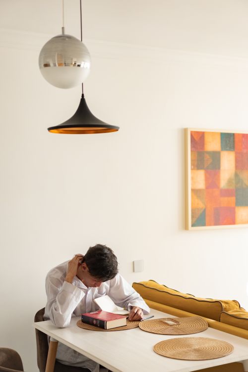 Free Man in white shirt deeply engaged in reading a book at a minimalist table setup. Stock Photo