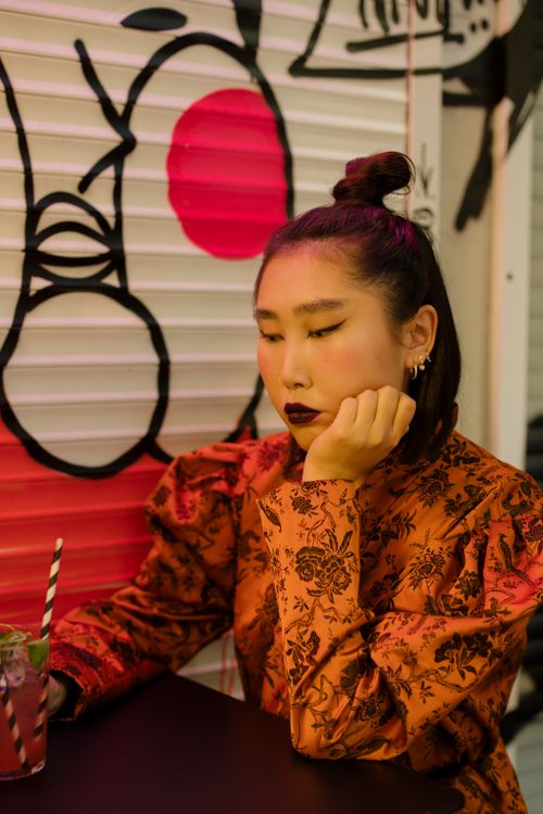 Free Woman in a fashionable red dress seated in a trendy café, lost in thought with a cocktail in hand. Stock Photo