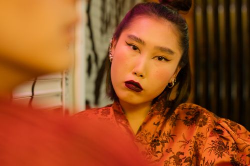 Free Close-up of a fashionable Asian woman indoors with dark lipstick and elegant dress. Moody lighting enhances style. Stock Photo