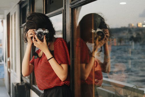 Woman in casual clothes standing near windows on ship deck while taking pictures on camera