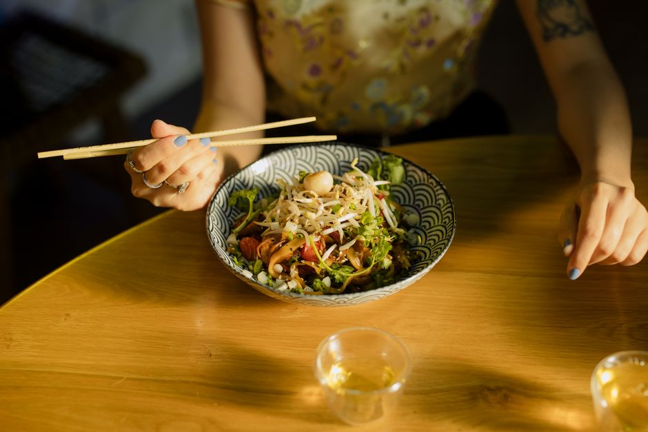 Individual savoring Asian fusion salad with chopsticks at a cozy indoor setting.