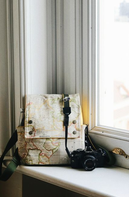 Vintage photo camera and backpack placed on white windowsill near window in daylight