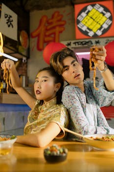 Young couple enjoying noodles in a vibrant Asian restaurant setting, capturing a moment of joy and togetherness.