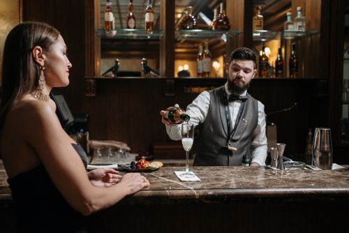 Free Bartender pouring drink for woman at a classy bar, elegant evening ambiance. Stock Photo
