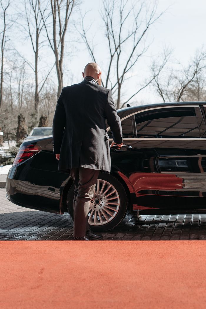 Chauffeur privé en costume ouvrant la porte d'une berline noire sur tapis rouge