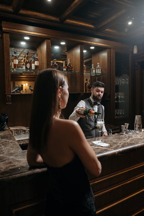 A Bartender Behind Bar Counter Pouring Wine in a Glass Near a Person