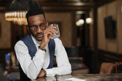 A well-dressed man holding a glass, exuding sophistication in a dimly lit upscale bar setting.