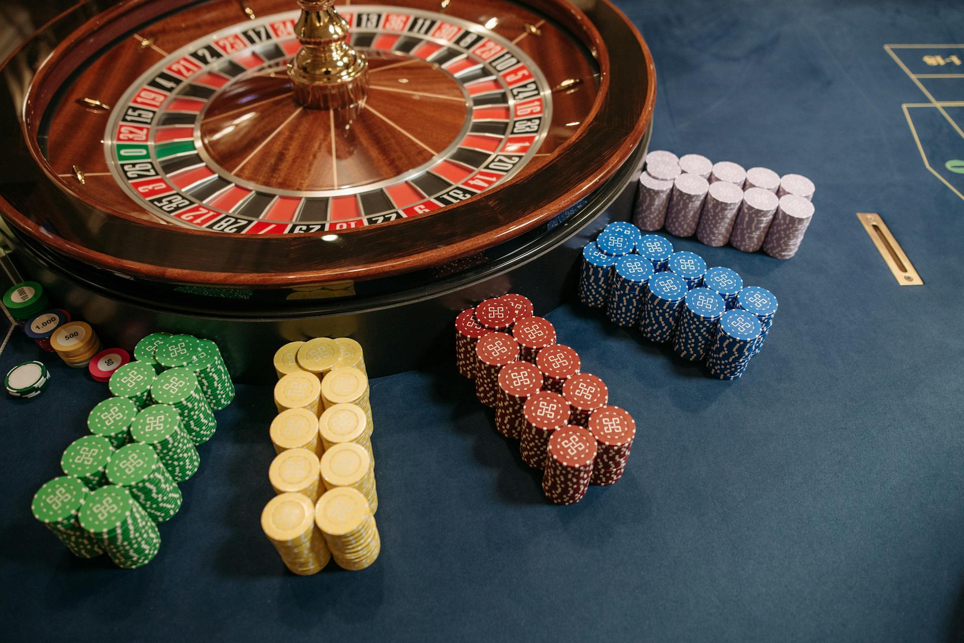 Vibrant poker chips stacked beside a roulette wheel in a casino setting.