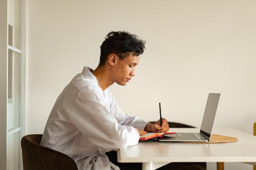 A Man Writing on a Notebook while Studying