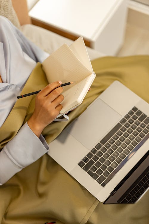 Free A Person Writing on the Notebook While Using a Laptop Stock Photo