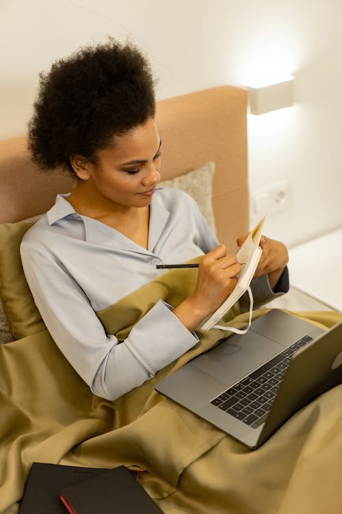 Free A Woman Writing on the White Notebook While Using a Laptop Stock Photo