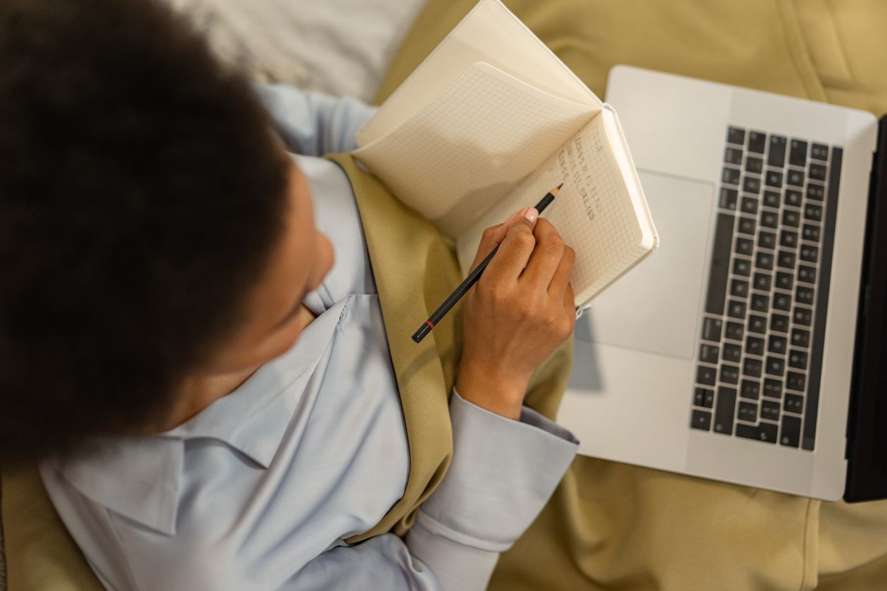 Hands writing in a notebook beside an open laptop, planning a course of study