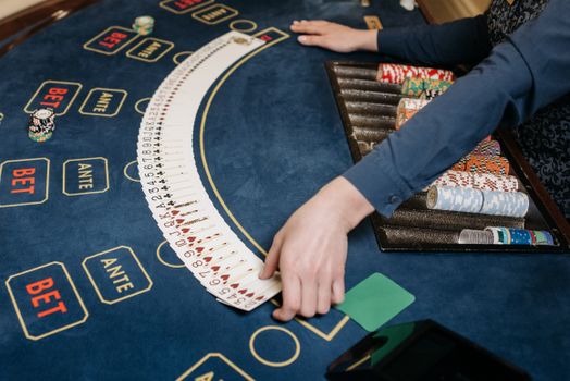 A casino dealer organizing playing cards on a gaming table with chips. Indoors setting.