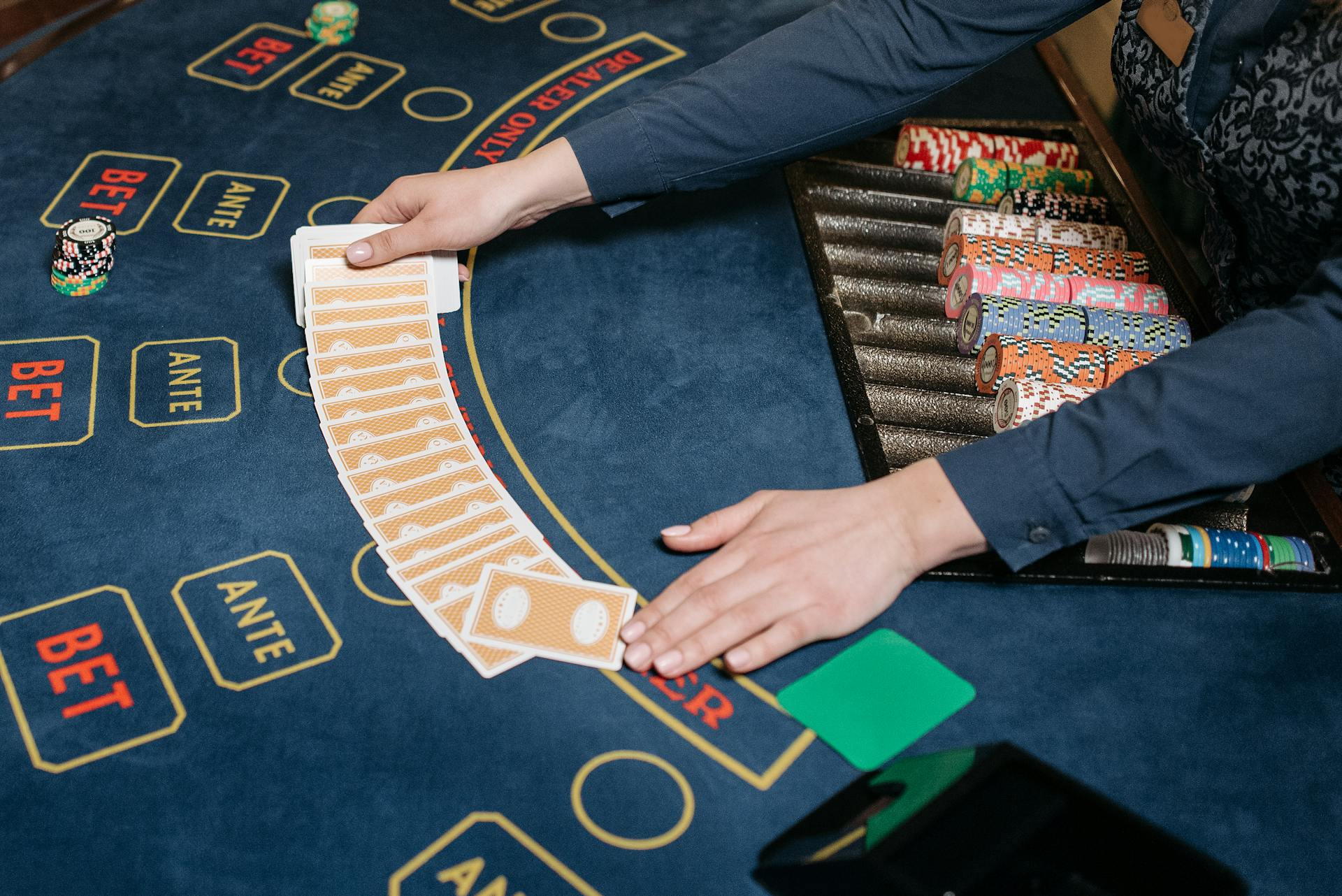 A casino dealer skillfully spreads playing cards on a gaming table, surrounded by colorful poker chips.