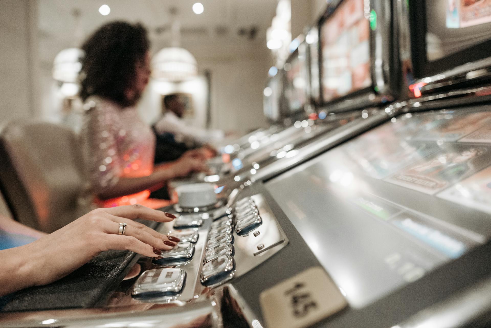 Close-up view of hands playing slot machines in a casino setting.