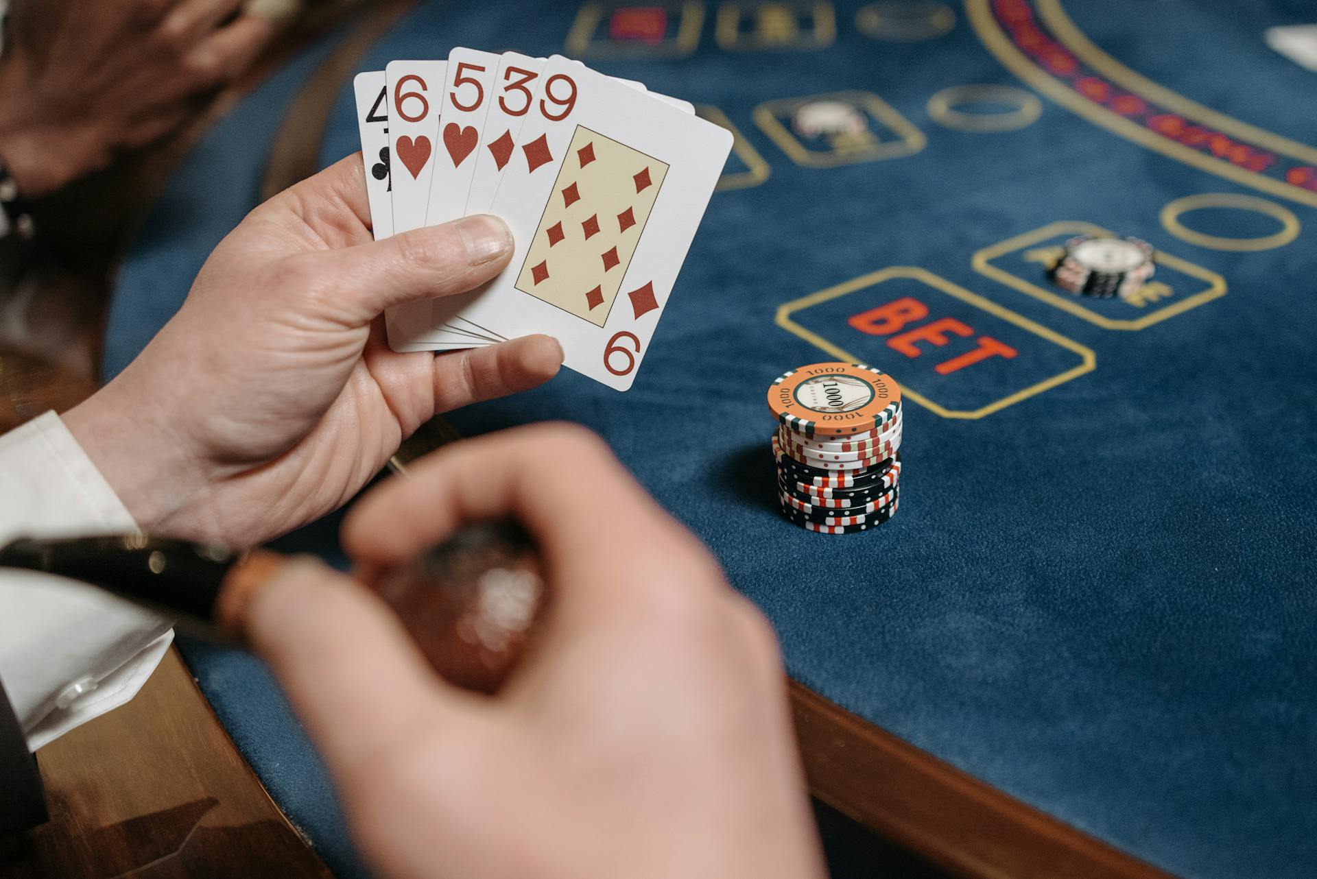 A gambler holding cards at a casino table filled with gaming chips.