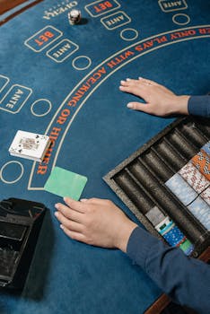 Casino table with dealer's hands, cards, and chips in a gambling setting.