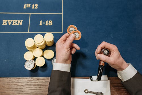 Person Holding a Poker Chips and Tobacco Pipe