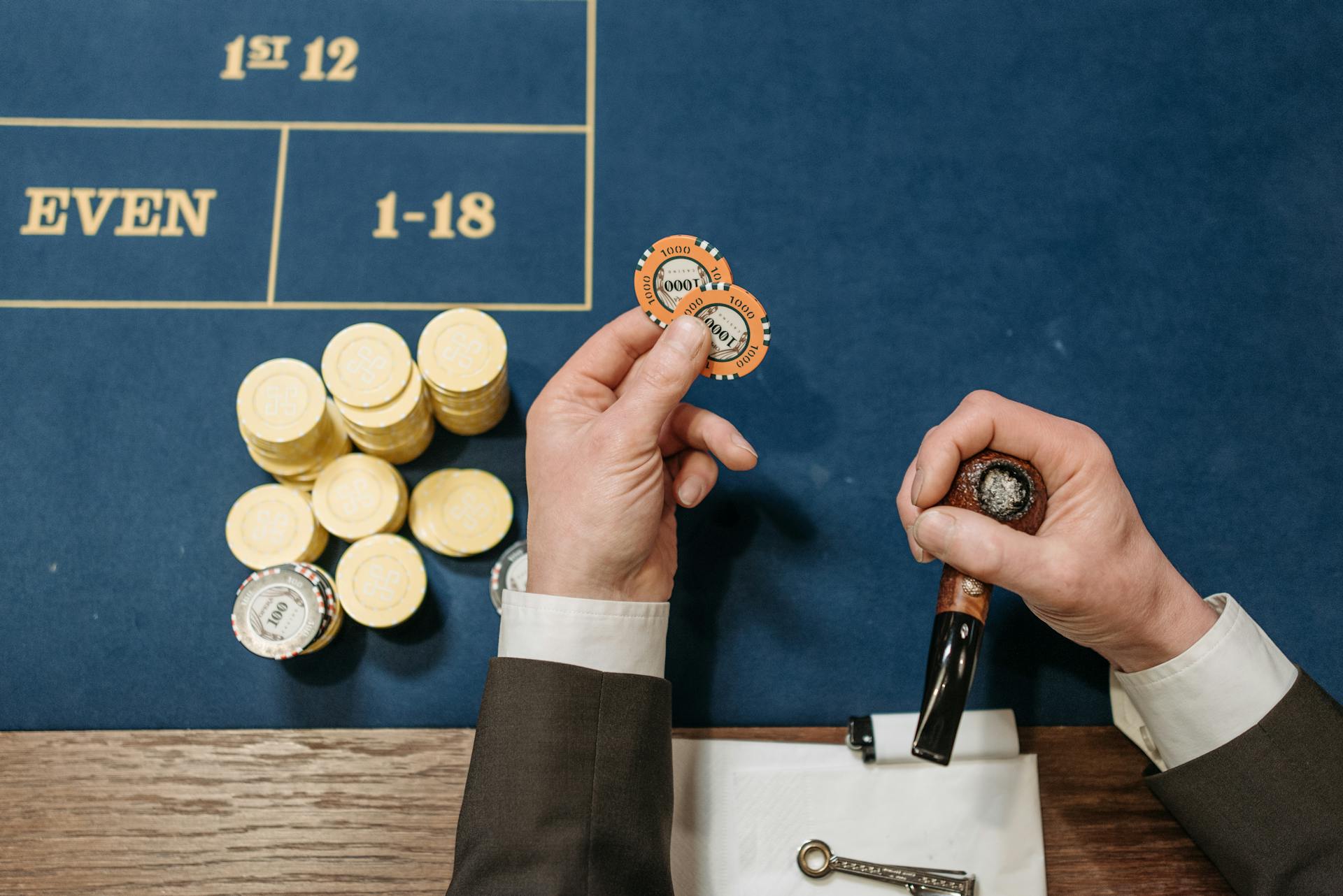 Overhead view of a casino table with poker chips and a tobacco pipe, depicting a gambling scene.