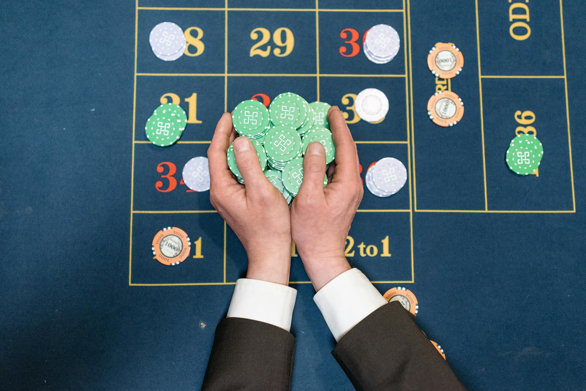 Hands in a suit holding poker chips on a casino gaming table.