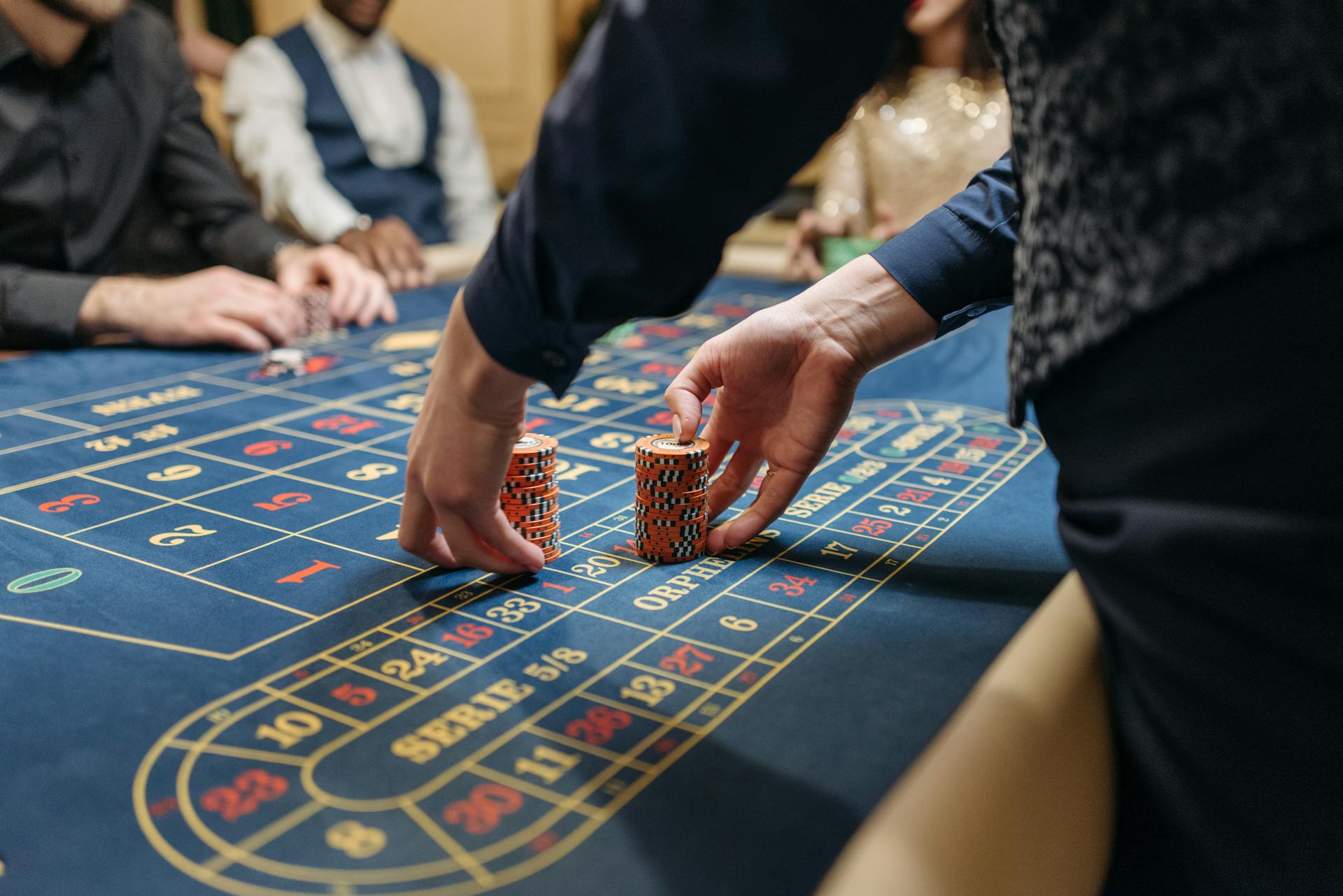 Close-up of players placing poker chips on a blue roulette table in a casino setting.