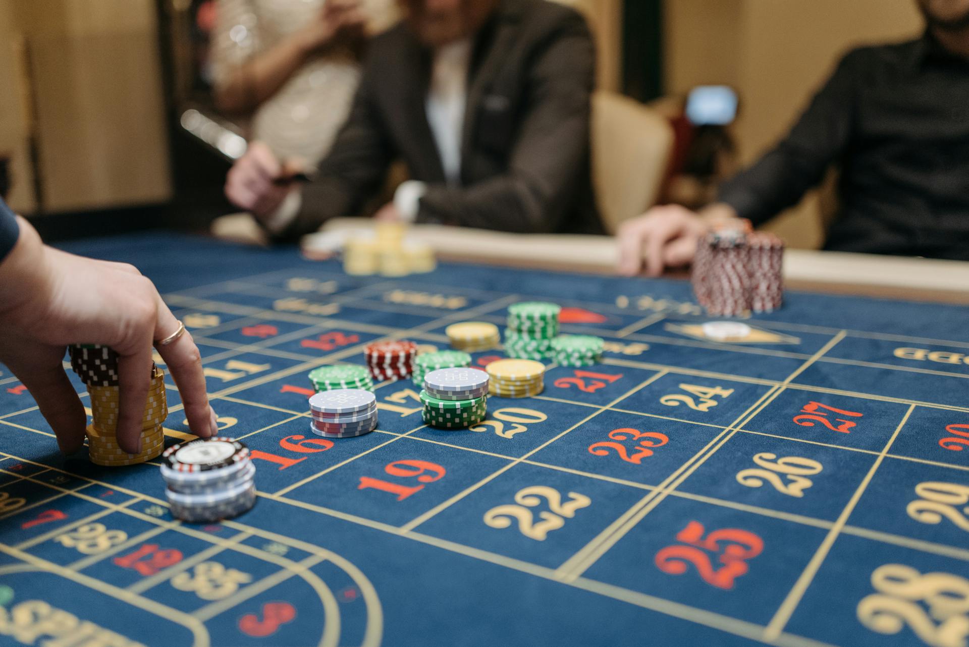 Hands placing betting chips on a roulette table in an upscale casino setting.