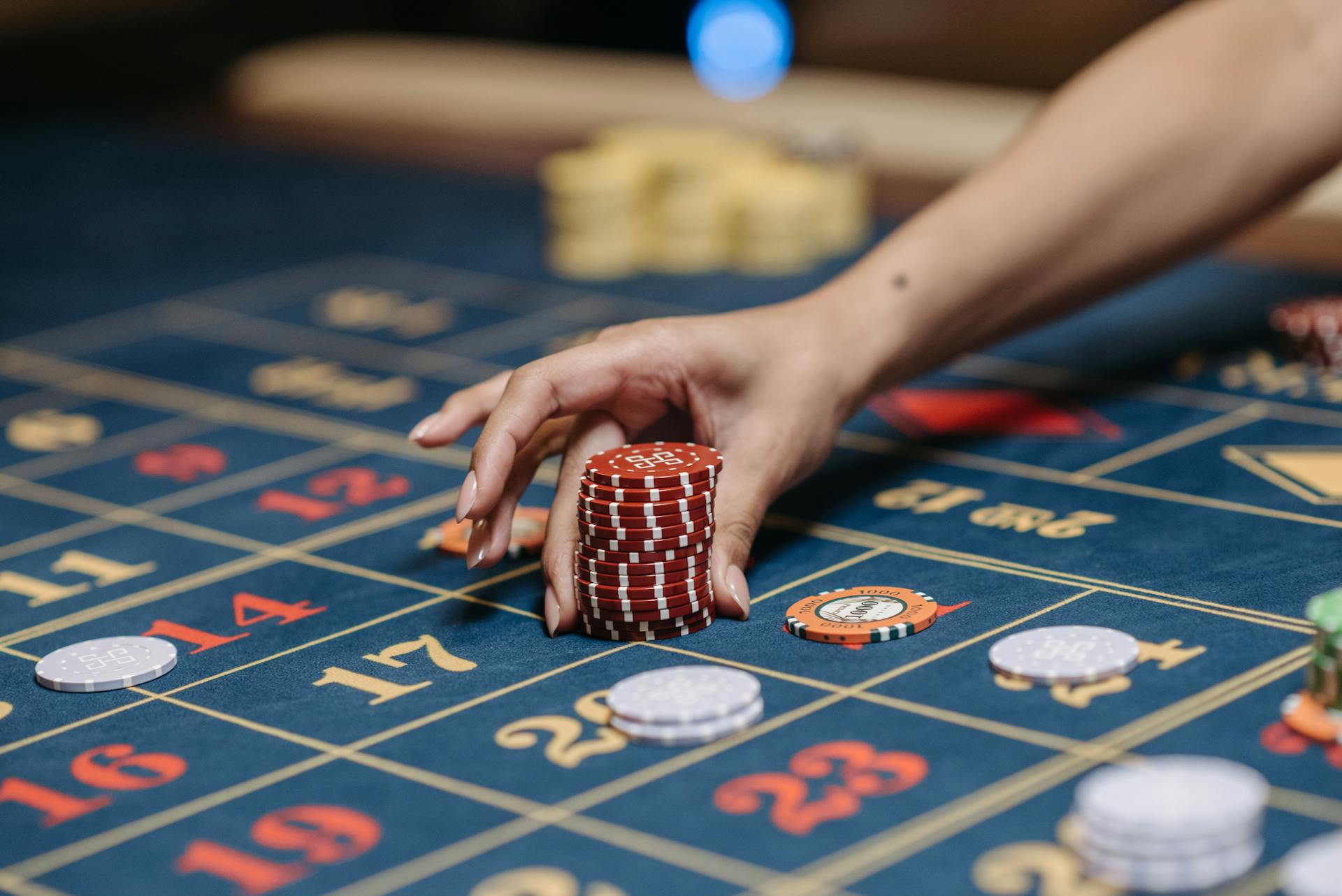 A hand holding poker chips on a roulette table, showcasing gambling and casino gaming.