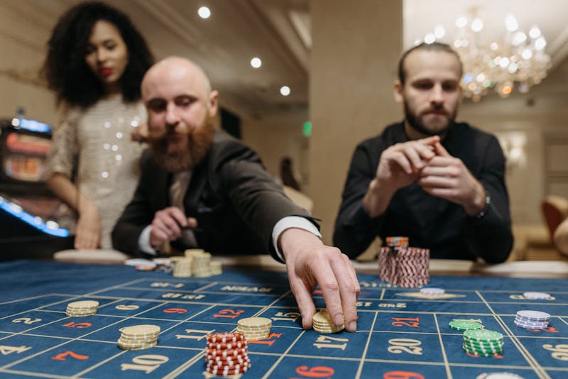 Three adults playing roulette at a casino, focused on placing bets with gaming chips.