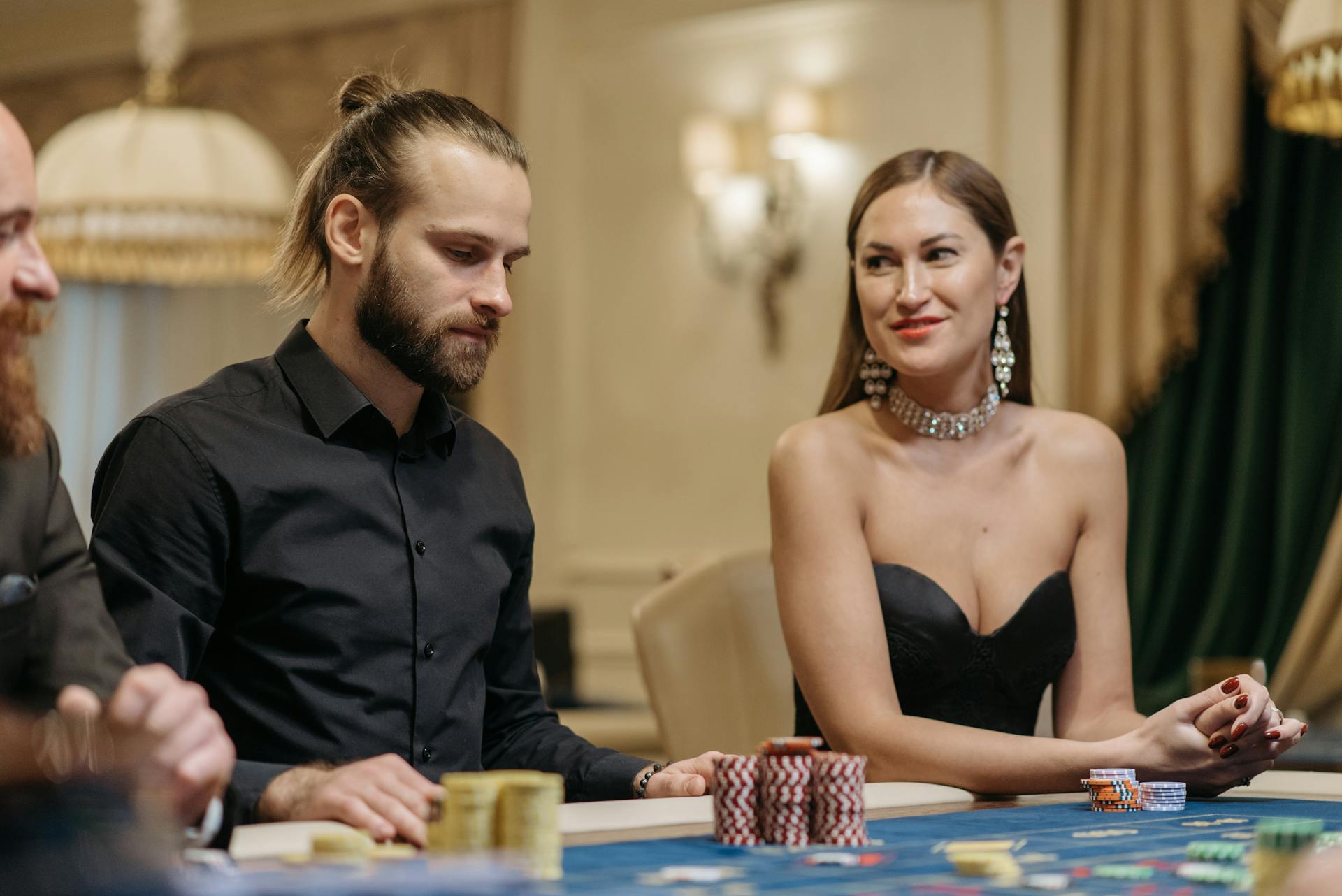 Man and woman sitting together at a casino gaming table with poker chips, exuding elegance and leisure.