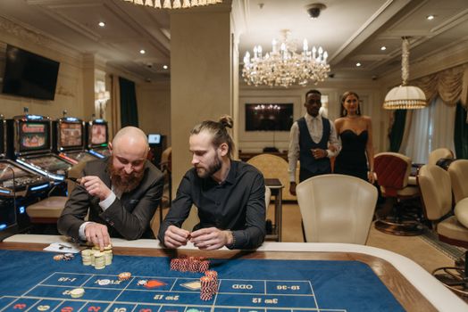 Elegant gamblers enjoy a night at the casino roulette table surrounded by luxury.