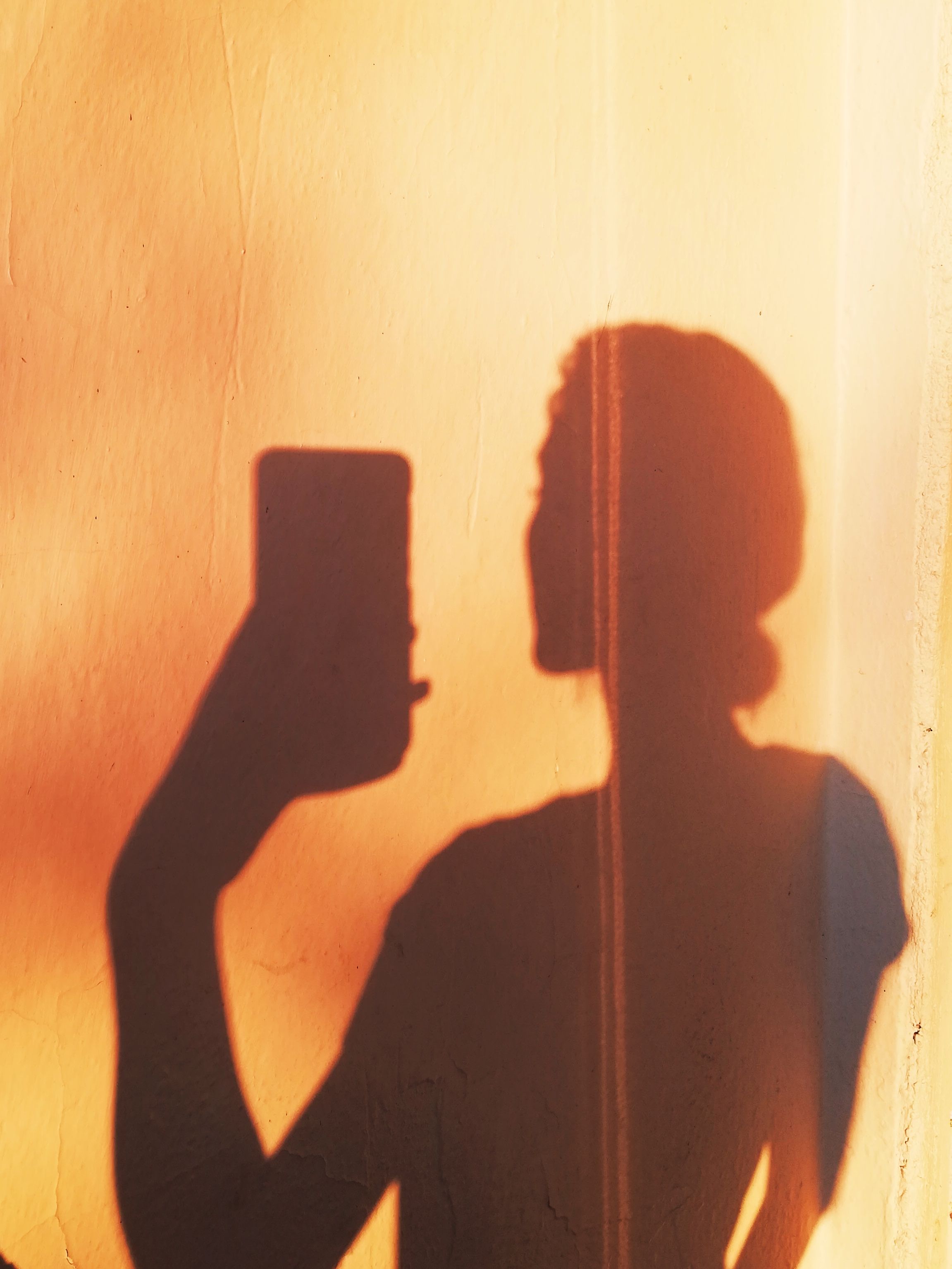 Shadow of a woman holding a phone against a wall during golden hour, creating a dramatic effect.