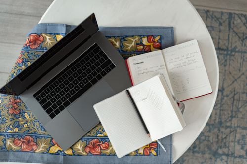 Free Overhead shot of a laptop with notebooks and a pencil on a patterned cloth. Stock Photo