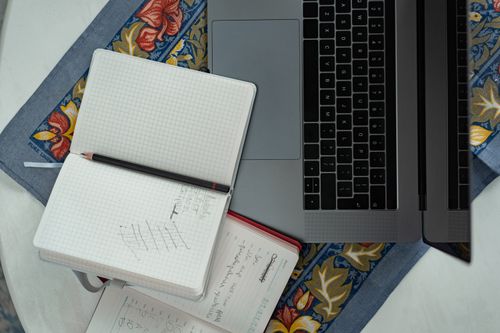 Free Flat lay of a laptop, notebooks, and a pencil on a floral tablecloth, ideal for productivity themes. Stock Photo