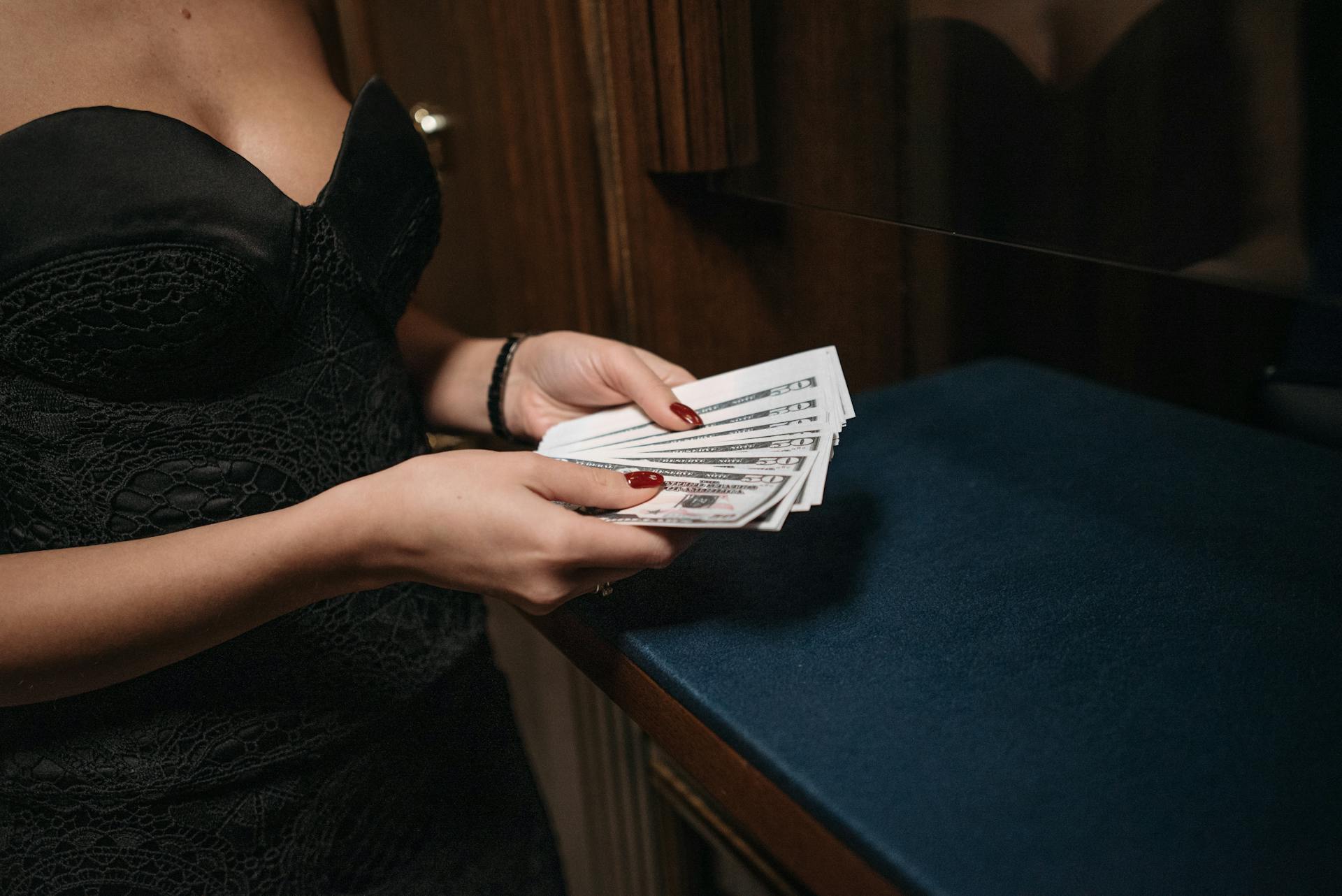 Woman in elegant dress holding money, showcasing wealth and luxury in an indoor setting.