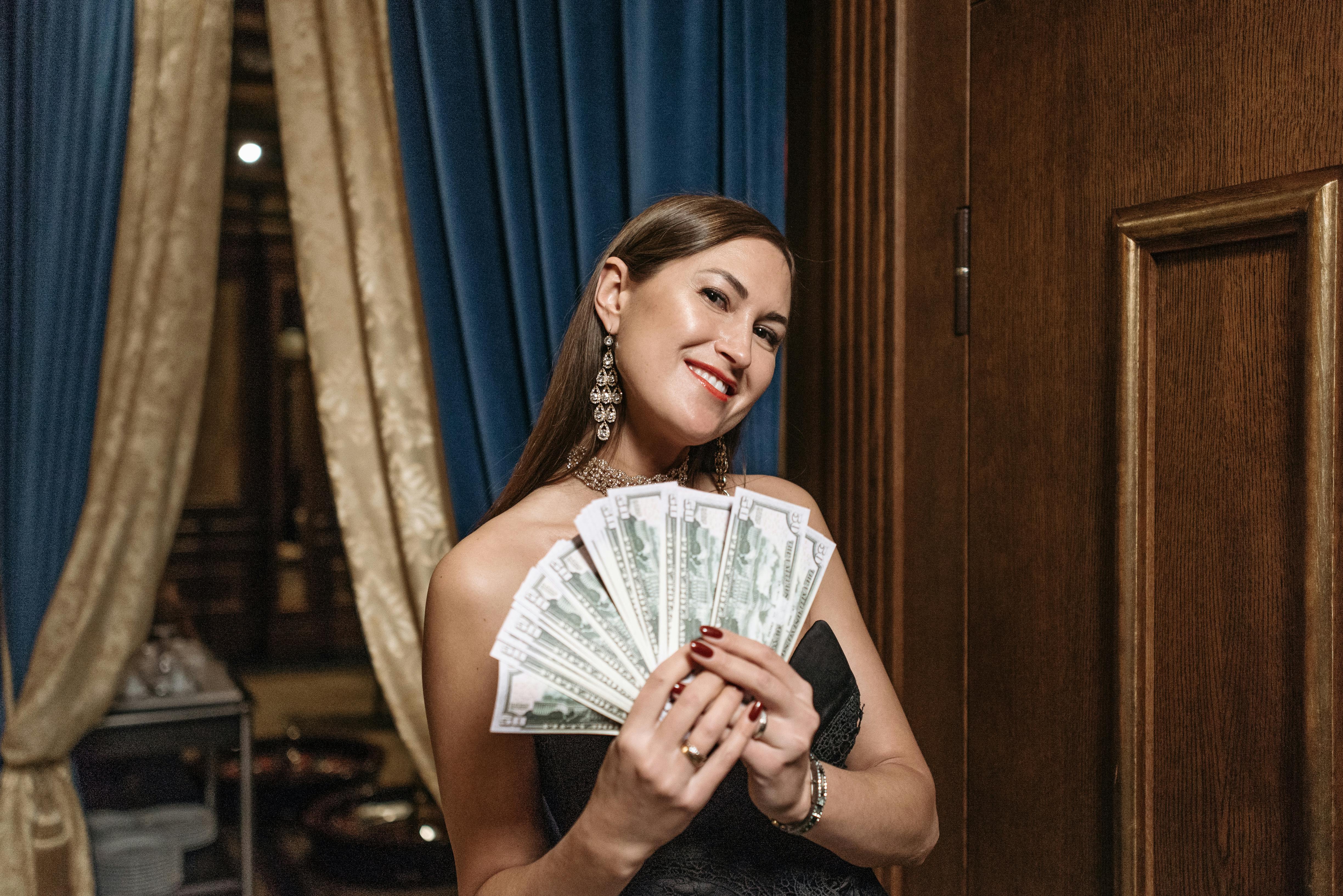 A woman in a glamorous setting holds a fan of cash, exuding confidence and wealth.